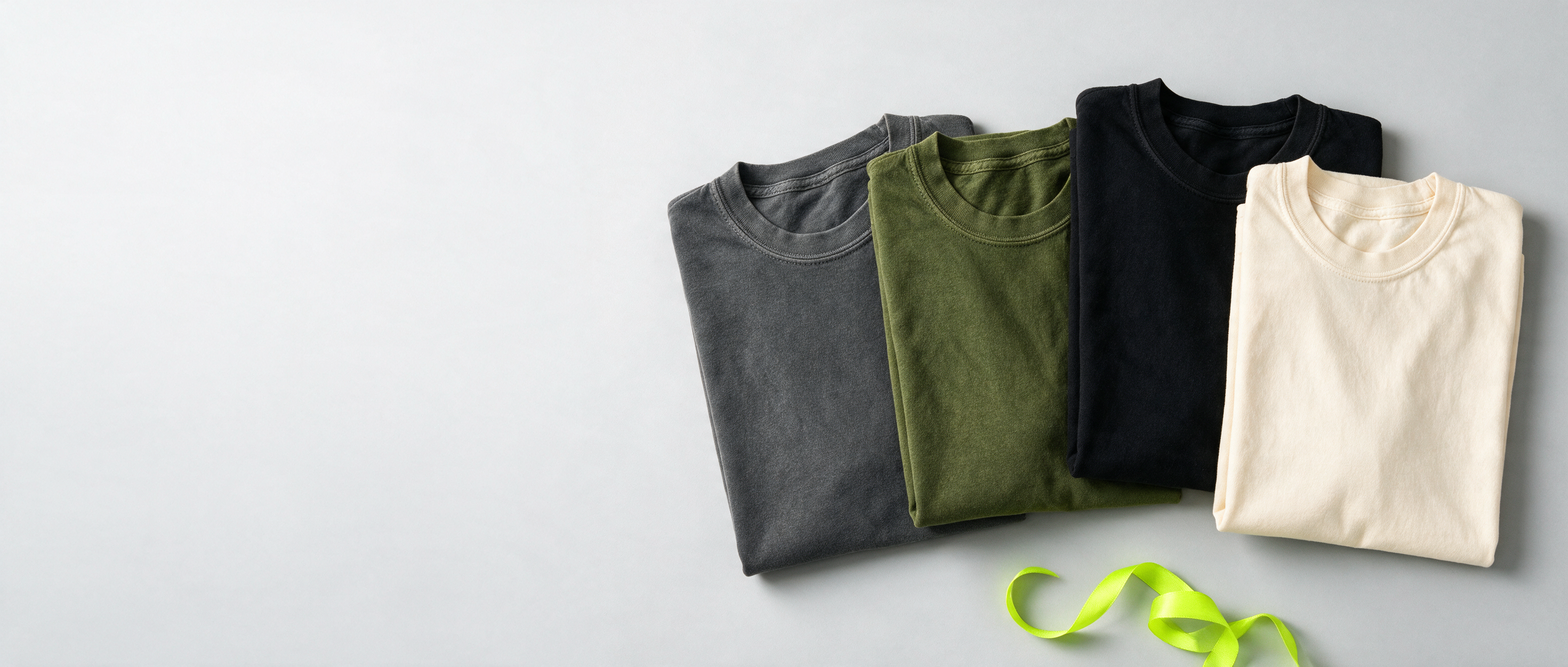 Flat-lay of folded garment-dyed tees with a lime ribbon